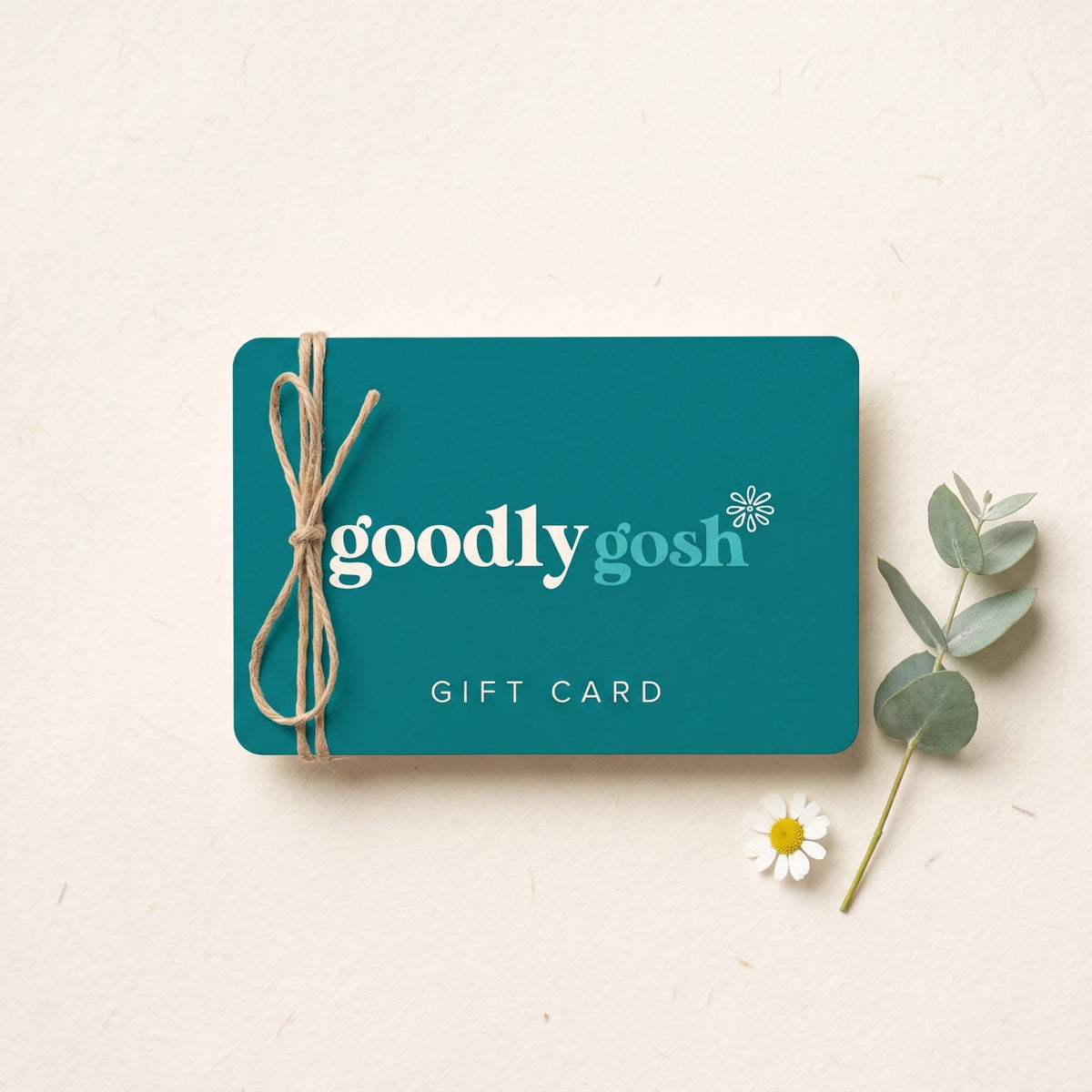 Goodly Gosh gift card in teal with cream logo, tied with jute twine beside eucalyptus and a daisy